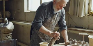 经验丰富的男陶工在小车间里用专业的设备、工具和许多陶俑在工作台上混合和揉制粘土。