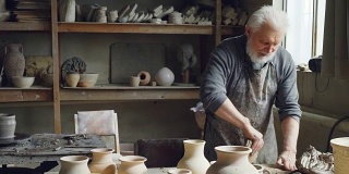 专业男性陶艺家在小作坊里，用陶艺设备、工具和许多陶艺人物，揉制陶土、捏制陶土球。