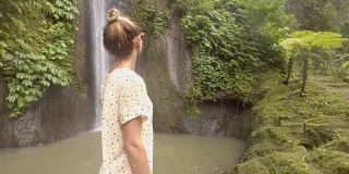 年轻女子在巴厘岛的瀑布上凝视大自然，享受大自然的新鲜。人们出行绿色环保理念。慢动作拍摄