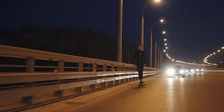 那家伙晚上骑着长板穿过城市。年轻人晚上在马路上滑冰。慢动作
