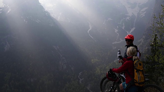 一对山地自行车夫妇停在悬崖边，向外看