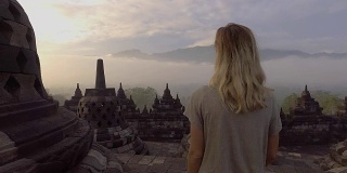 一名年轻女子在婆罗浮屠古代佛教寺庙日出时徘徊的4K视频。人们旅游发现亚洲的概念