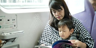 年轻的亚洲母亲和儿子在火车上看书。