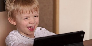 小男孩一边在平板电脑上看卡通片一边笑