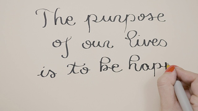 女性用黑墨水的笔在白纸上写下励志的信息，我们生活的目的是为了幸福