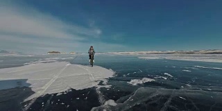 一个女人在冰上骑自行车。这个女孩穿着银色的羽绒服，背着自行车背包，戴着头盔。结冰的贝加尔湖的冰。自行车的轮胎上覆盖着特殊的尖钉。