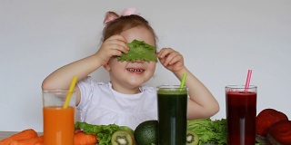 饮食、排毒、素食主义和健康生活方式的概念。小女孩喝蔬菜冰沙-胡萝卜，甜菜和绿色。一个可爱的婴儿吃莴苣叶