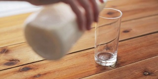 用手把牛奶倒进木桌上的玻璃杯里