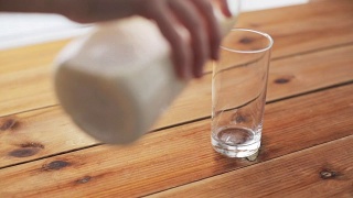 用手把牛奶倒进木桌上的玻璃杯里视频素材模板下载