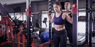 年轻的亚洲肌肉女性举下蹲杠铃在健身房，生活方式运动和健美的概念