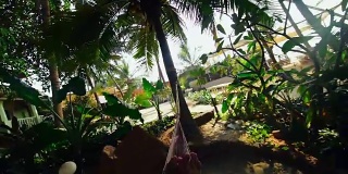 男性的双腿在热带棕榈树的吊床上摇摆着