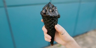 蓝色背景上女性手握黑色木炭冰淇淋