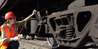 一位年轻的女铁路工人正在检查货车的悬挂装置。