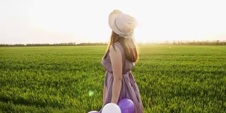 美丽的女孩拿着五颜六色的气球走在春天的田野上