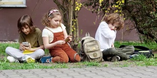 放学后，小学生们坐在草地上，从书包里拿出智能手机，玩网络游戏。网络成瘾。视频游戏