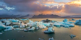 4k时间推移日落场景移动的云与蓝色冰山漂浮在Jokulsarlon冰川泻湖，冰岛