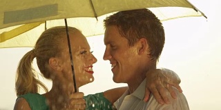 近距离观察:春雨中，一对美丽的年轻夫妇在伞下旋转。