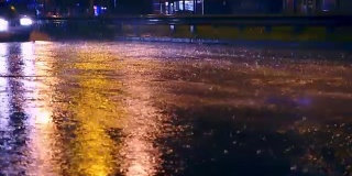 在城市的夜间道路上，汽车开进大水坑，车轮下溅起水坑