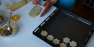 准备脆饼。女人把面团擀开，撒上芝麻。接下来，在烤盘上放好饼干的底座。