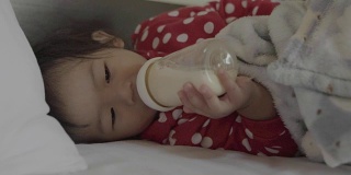亚洲可爱的小女孩喝奶瓶里的牛奶。