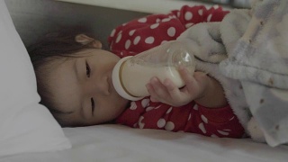 亚洲可爱的小女孩喝奶瓶里的牛奶。视频素材模板下载
