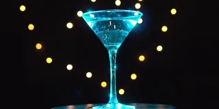 明亮的鸡尾酒在玻璃中，旋转和改变颜色在黑暗的背景和模糊的光。