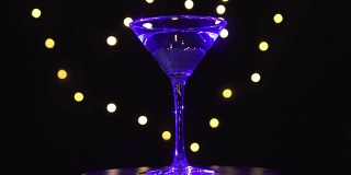 杯中的亮蓝色鸡尾酒，在昏暗的背景和模糊的光线下旋转。