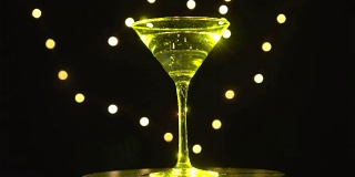 玻璃杯中的亮黄色鸡尾酒，在昏暗的背景和模糊的光线下旋转。