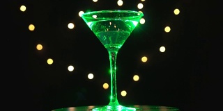 明亮的绿色鸡尾酒在玻璃中，旋转在黑暗的背景和模糊的光线。