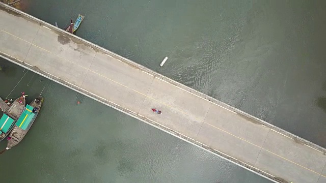 一名年轻女子骑着她的摩托车越过一座横跨热带河流的桥。