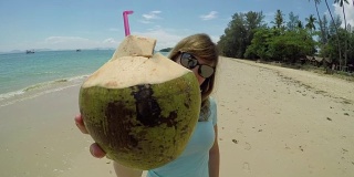 肖像:快乐的游客举起她的椰子，喝了一口可口的果汁。
