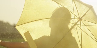 快乐的女人撑着伞旋转着，用手感受着雨