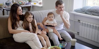 一个友好的家庭，一个男人，他的妻子和他们的孩子坐在客厅的沙发上看电视