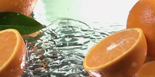 Orange hits orange juice surface and splits into halves. Slow motion shot