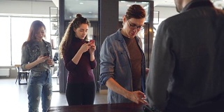 一名兴高采烈的顾客在咖啡馆用智能手机支付，而排队的顾客正在用手机等待。外卖饮料和现代银行概念。