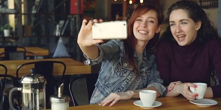 漂亮女孩最好的朋友是用智能手机自拍，然后在咖啡馆喝咖啡的时候看照片。友谊，社交媒体和拥有乐趣的概念。