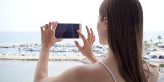 一个女人在阳台上用手机。女性喜欢看海，用手机慢动作拍照