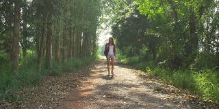 快乐的年轻亚洲女子旅行者背包行走在森林。徒步旅行者亚洲女人与背包走在夏季森林的路径。探险背包客的旅游理念。