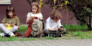 放学后，小学生们坐在草地上，从书包里拿出智能手机，玩网络游戏。网络成瘾。视频游戏