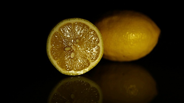 一片柠檬和一个多汁的柠檬放在深色镜子桌上。高清