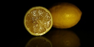 一片柠檬和一个多汁的柠檬放在深色镜子桌上。高清