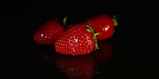 三颗草莓躺在深色的背景上。一滴水滴到草莓上