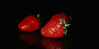 三颗草莓美丽地躺在黑色的桌子上，在一缕光线的背景下。高清