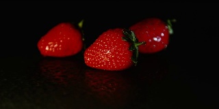 黑暗中，潮湿的地面上放着三个草莓。黑色背景