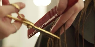女性手发型师梳理长发，用理发剪刀剪发。近距离的女人美发与专业剪刀在美容院