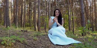 穿着蓝色长裙的漂亮女人在森林里吃苹果