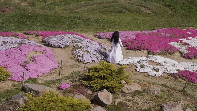 美丽的女人走过粉红色的花坛