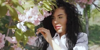 漂亮的黑发女人闻着樱花