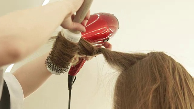 理发师在美发后用刷子和吹风机做长发造型。靠近发型师，用吹风机和发刷吹干长发。在美容院做完头发