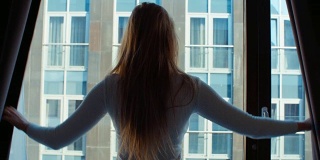 年轻女子拉开窗帘向窗外望去的剪影。